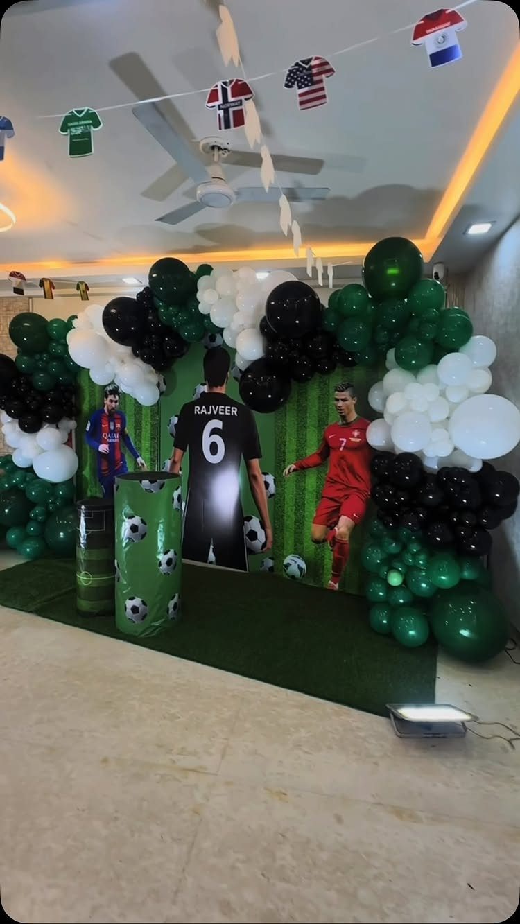 Football party backdrop with green, black, and white balloons and player cutouts.