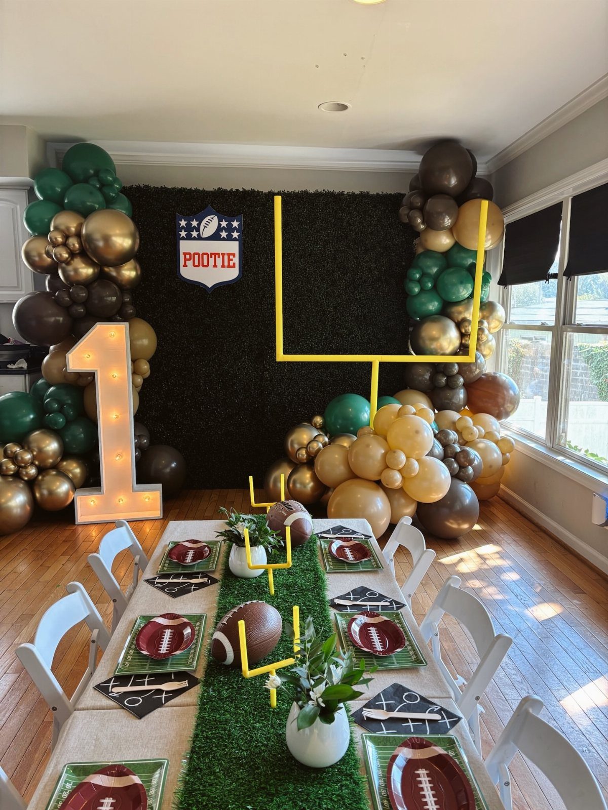 Football themed first birthday party setup with green balloons and grass table runner