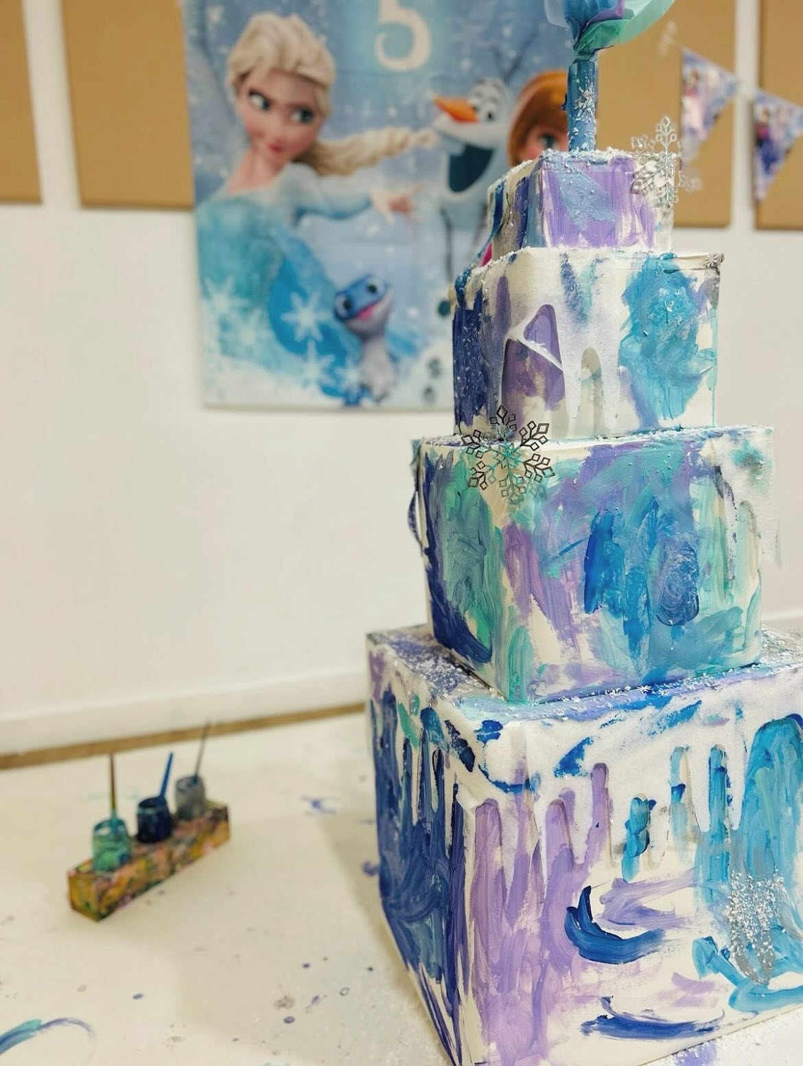 Three-tiered cake with blue and purple paint strokes and silver snowflake decorations.