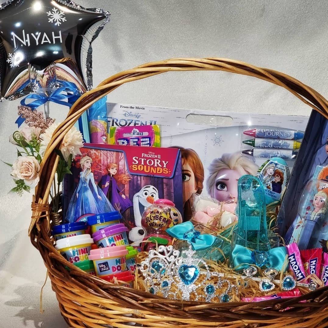 Wicker gift basket filled with Frozen themed toys, dolls, and a personalized balloon.