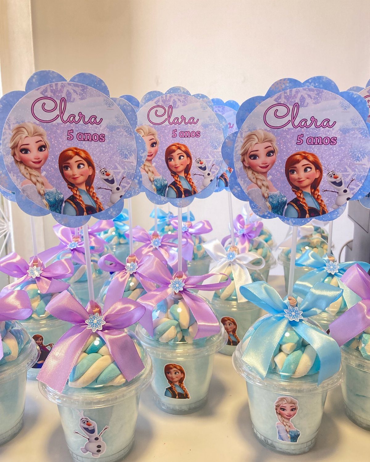 Frozen themed party favor cups with ribbons and character toppers for a birthday.