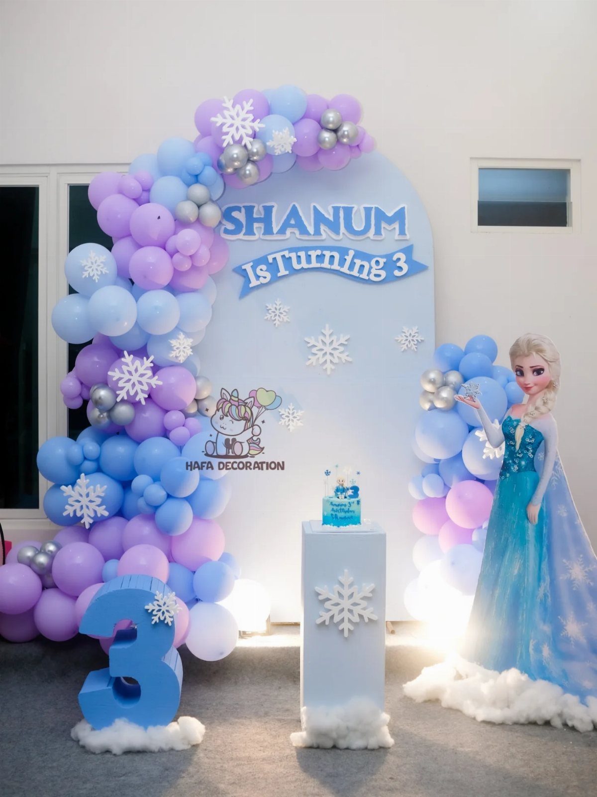 Birthday party backdrop with blue and purple balloons, snowflakes, and Elsa cutout.