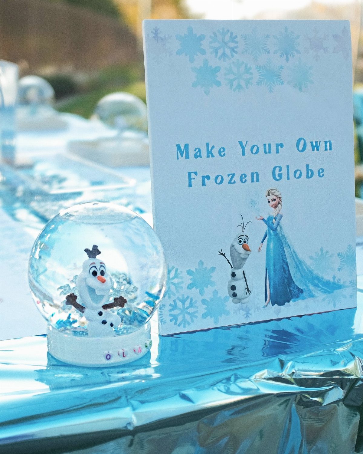 Olaf snow globe and a sign for making frozen globes on blue foil.