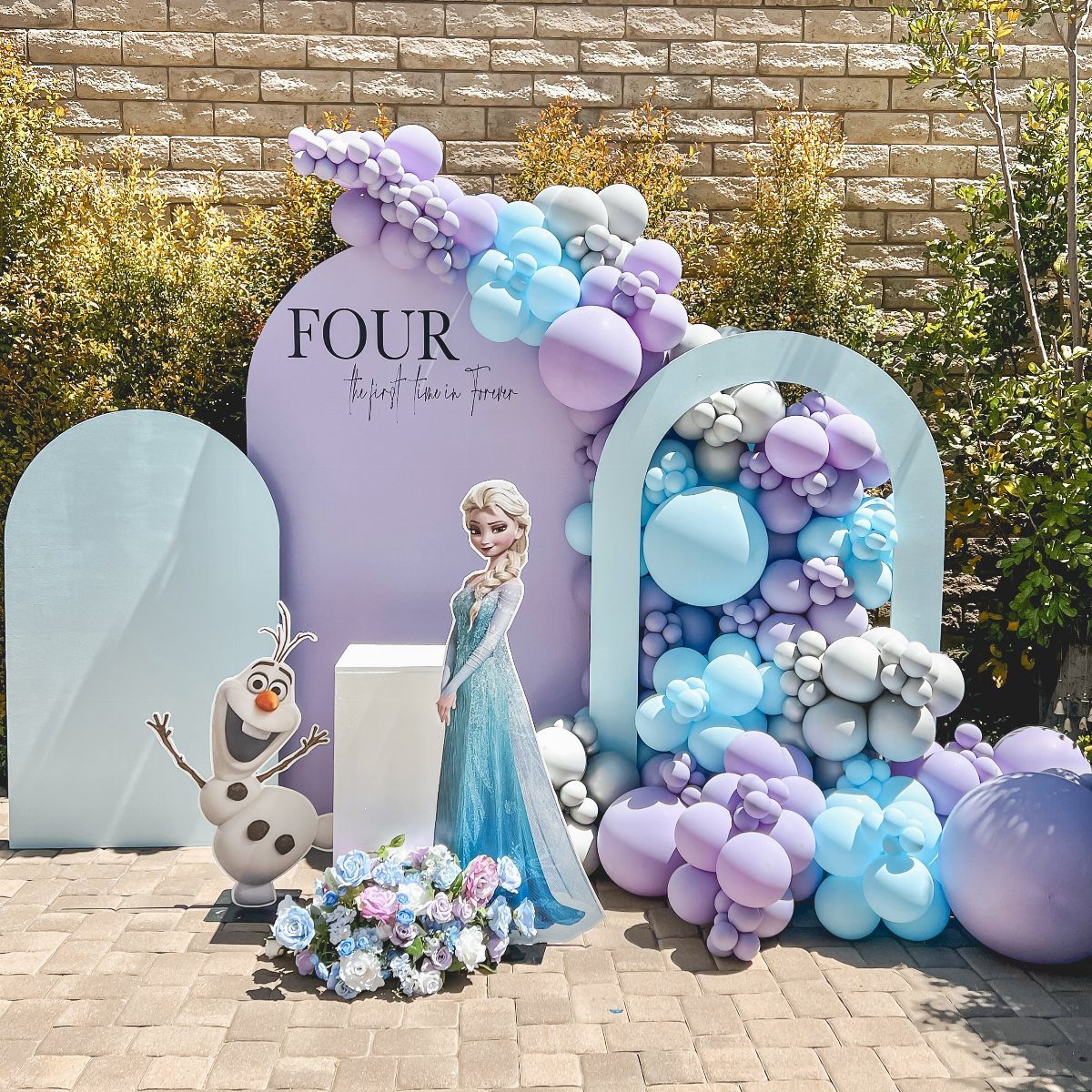 Elsa and Olaf standing before a blue and purple balloon party backdrop.
