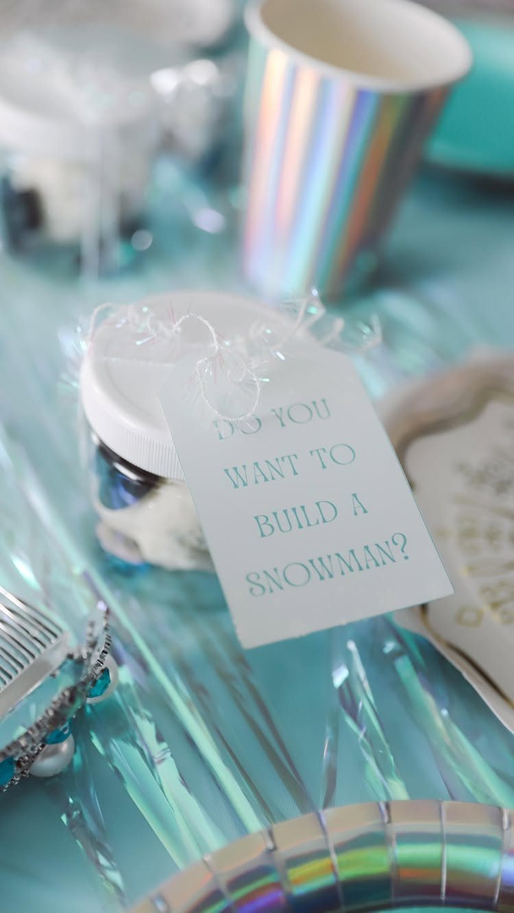 Jar of white marshmallows with a snowman themed tag on blue iridescent table