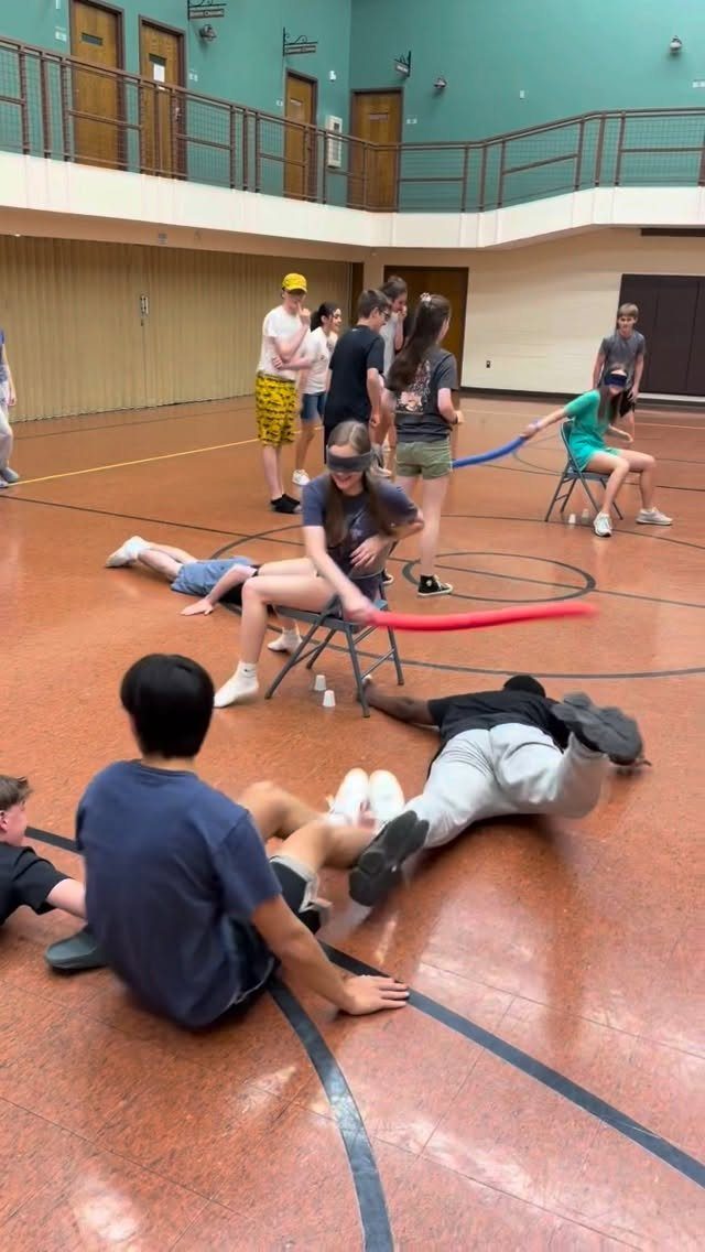 Teenagers playing a blindfolded foam noodle game in a school gymnasium