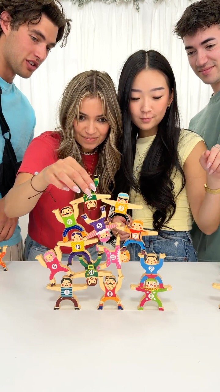 Teenagers stacking colorful human-shaped figures on a white table in a bright room.