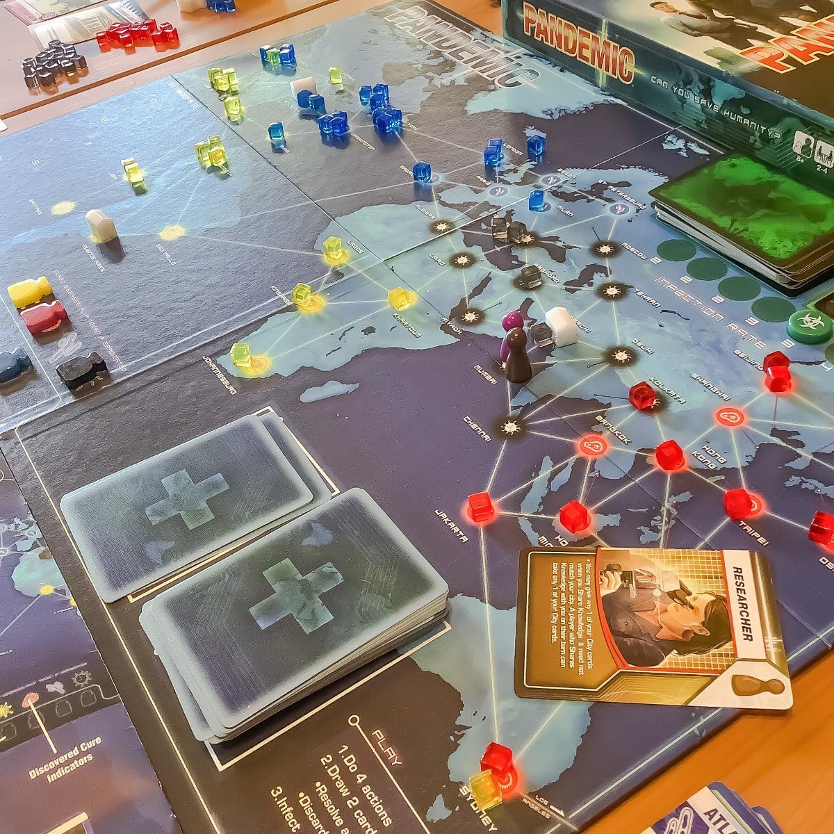 Pandemic board game setup with world map, colorful markers, and character cards.