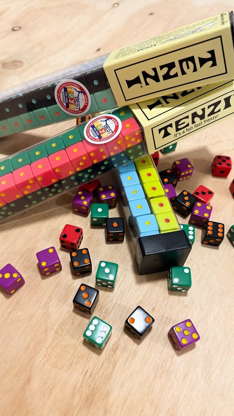 Tenzi game boxes and colorful dice scattered on a light wooden table