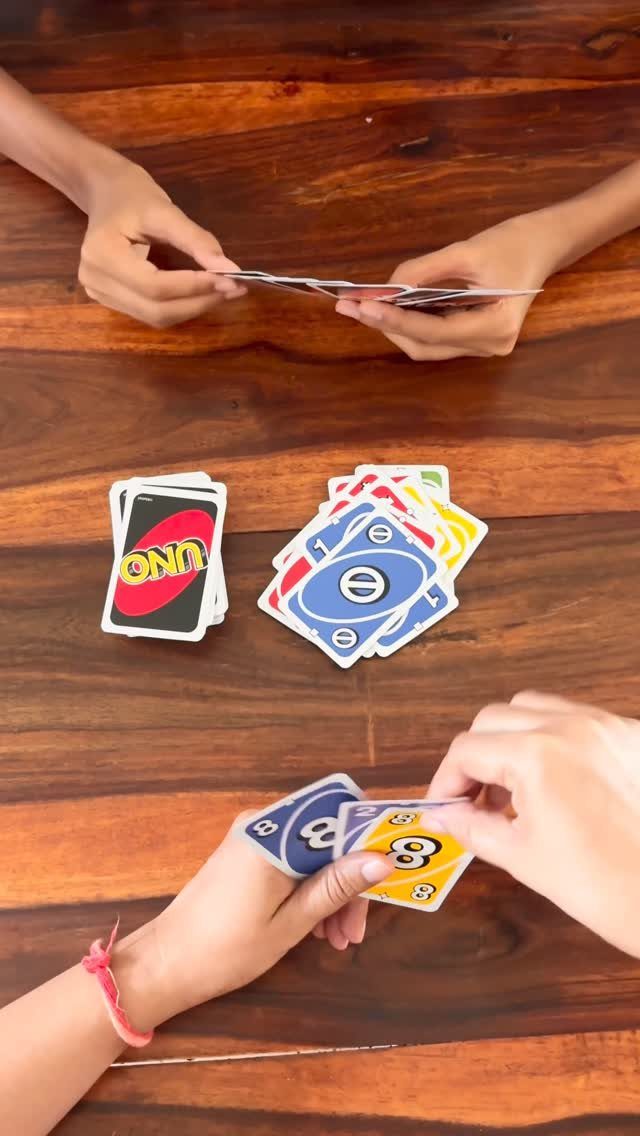 Hands of players holding and playing Uno cards on a wooden table.