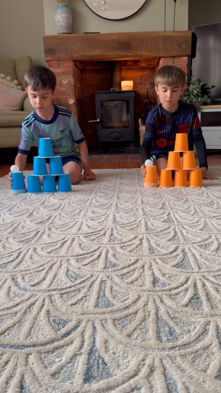 Two boys building pyramids of blue and orange plastic cups on a rug.
