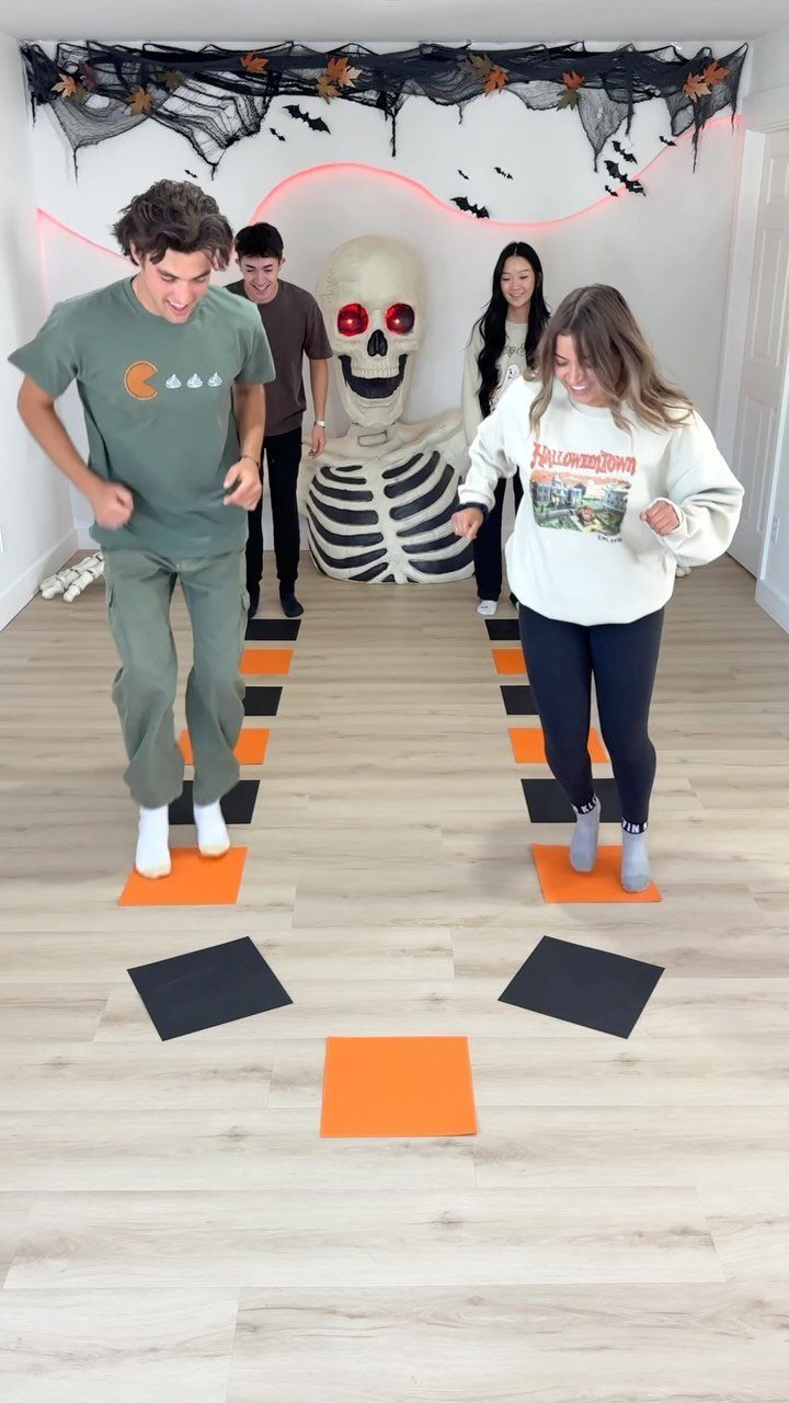 Young adults jumping on orange and black mats in a Halloween themed room