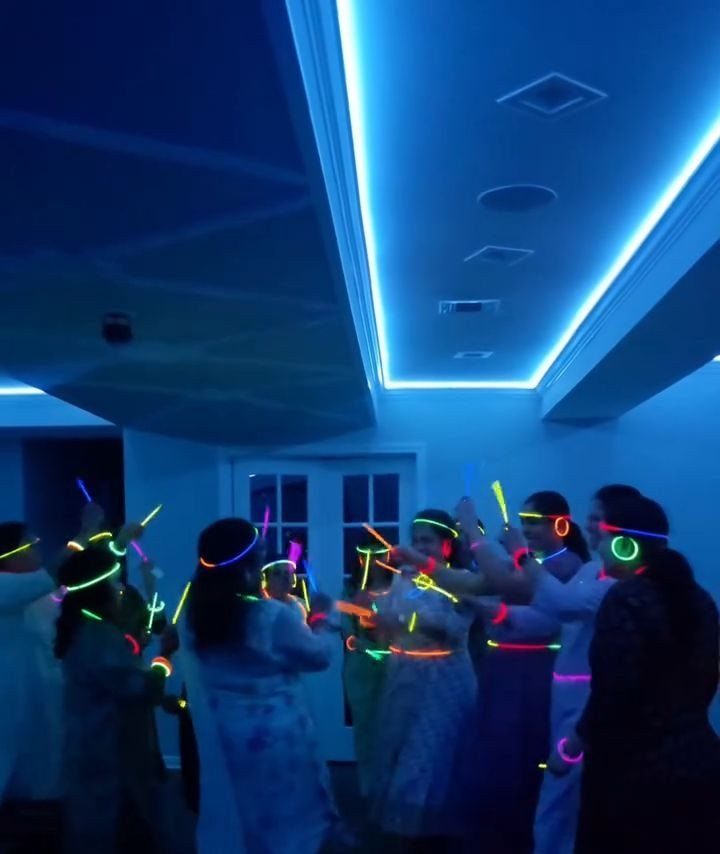 People wearing glowing neon accessories dancing in a room with blue lighting.