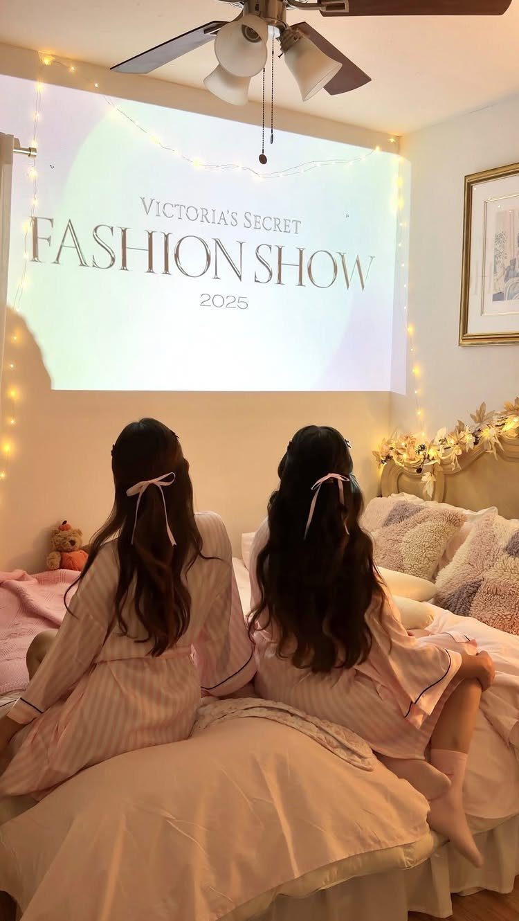 Two girls in pajamas watching a fashion show projected on a bedroom wall.