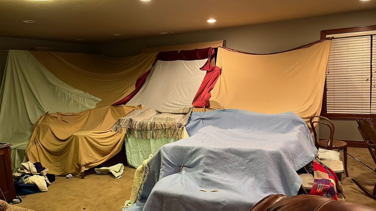 Large indoor fort made of colorful blankets and sheets draped across a room.