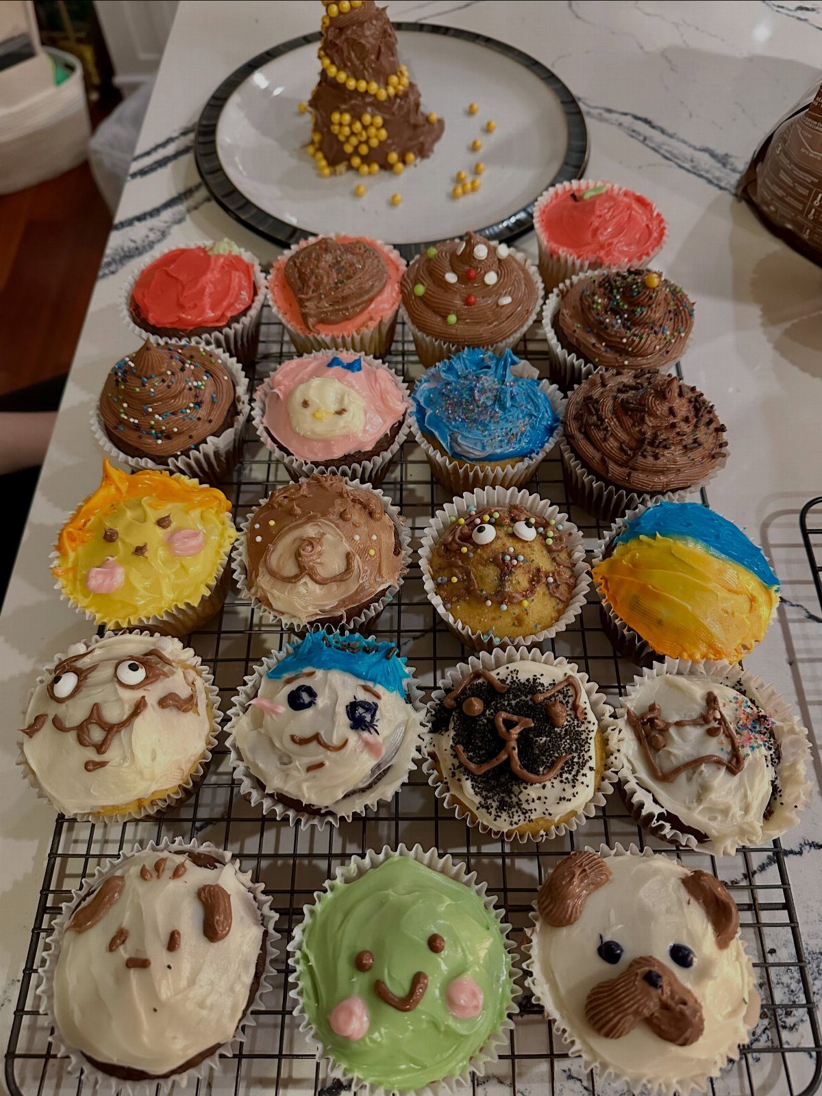Decorated cupcakes with colorful frosting and animal faces on a wire cooling rack.