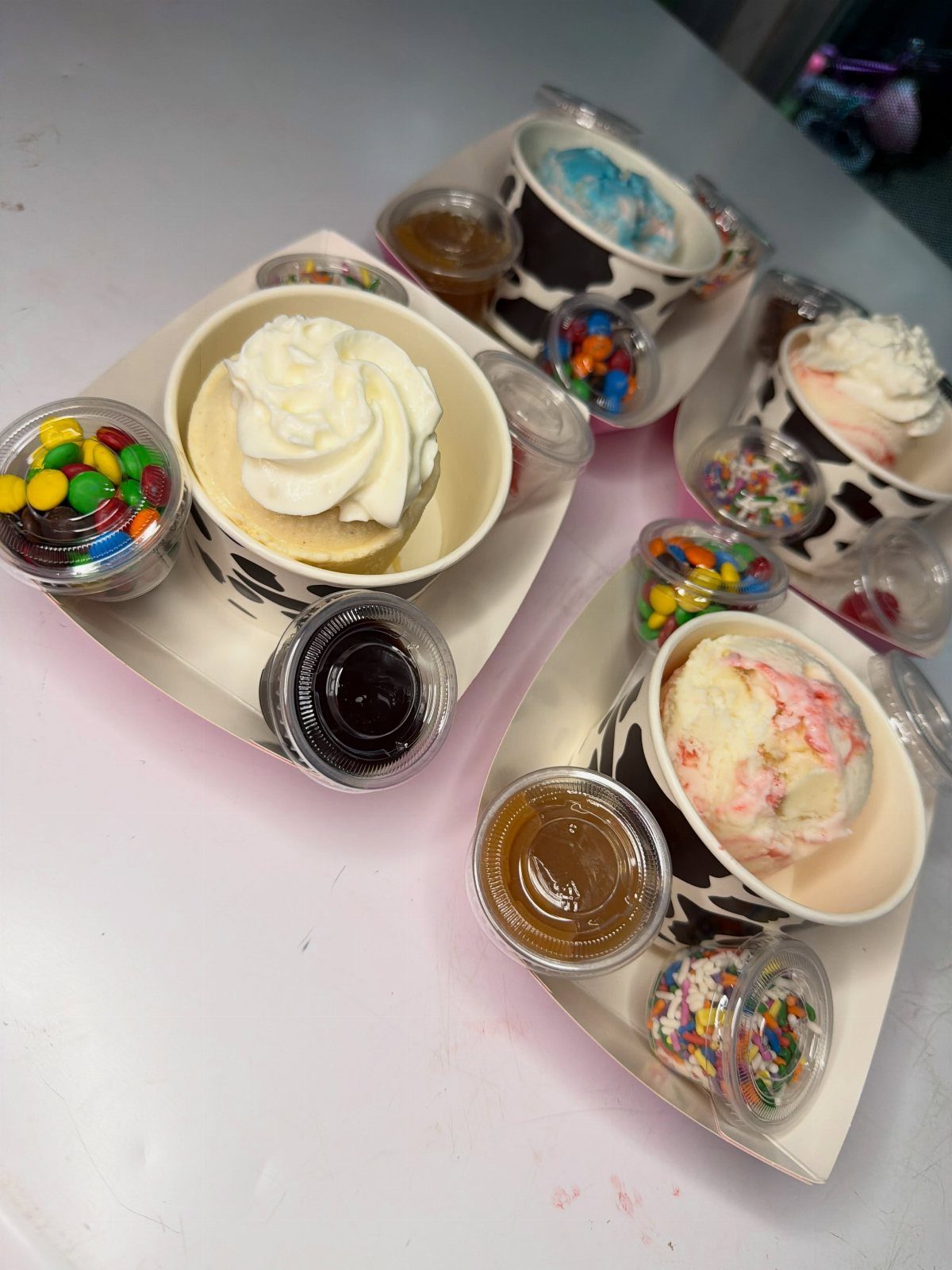 Ice cream sundaes in cow-print cups with colorful candy and syrup toppings.