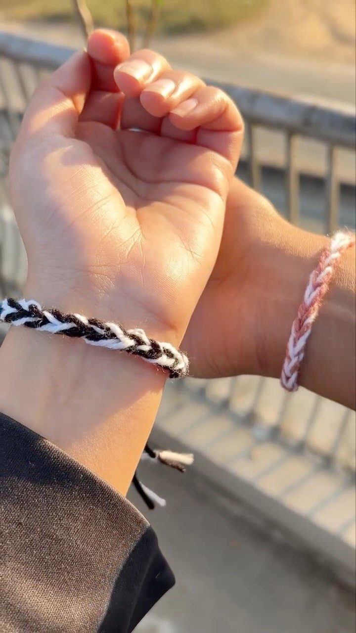 Two wrists wearing braided black, white, and pink friendship bracelets outdoors.