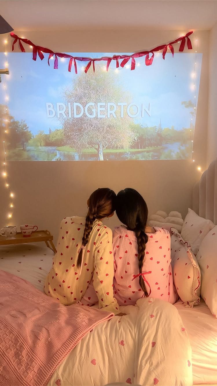Two girls in pajamas watching a movie projected on a bedroom wall.