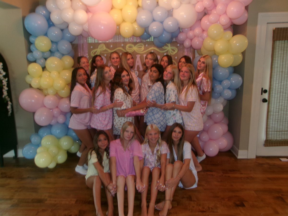 Teenage girls in pajamas posing before a colorful pink, yellow, and blue balloon arch.