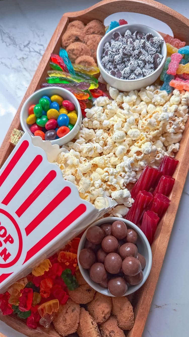 Wooden snack tray with popcorn, colorful candies, chocolate balls, and gummy sweets.