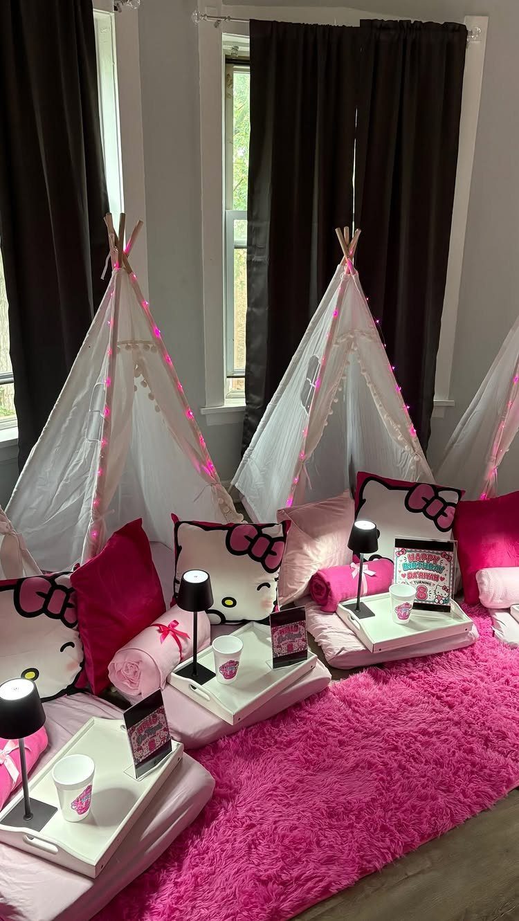 White teepee tents with pink pillows and fairy lights on a pink rug.
