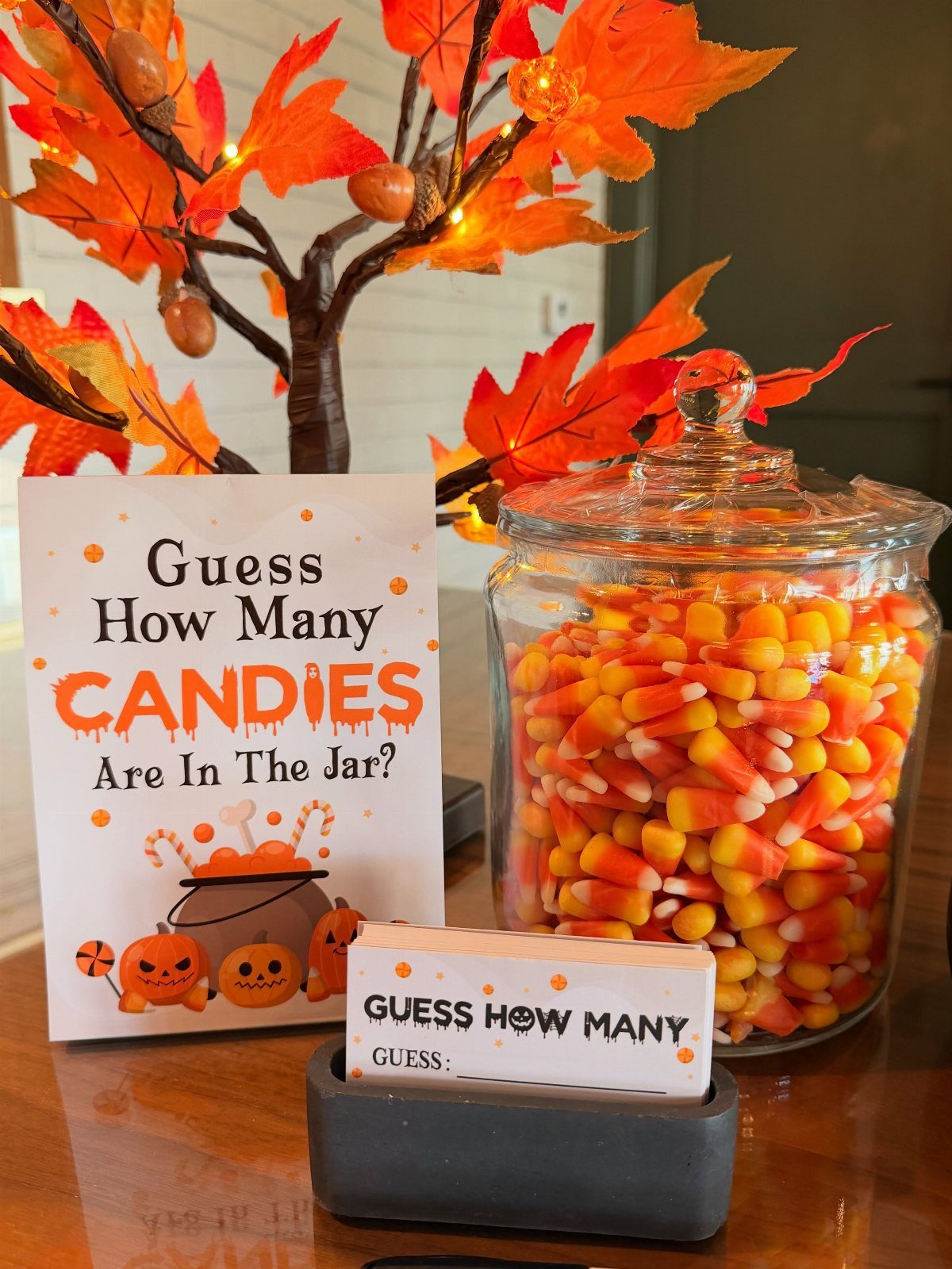 Glass jar filled with candy corn next to a guessing game sign.