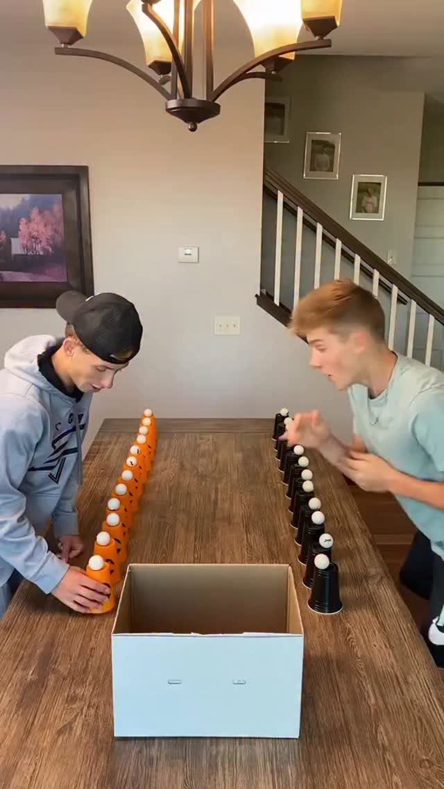 Two teenage boys playing a cup game with orange and black cups on a table