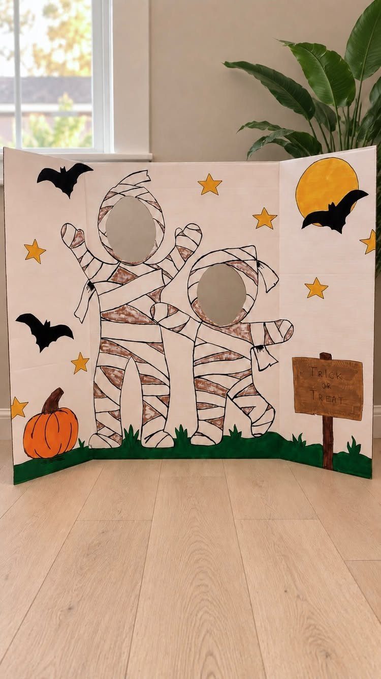 Cardboard photo booth backdrop with mummy face cut-outs, bats, and a pumpkin.