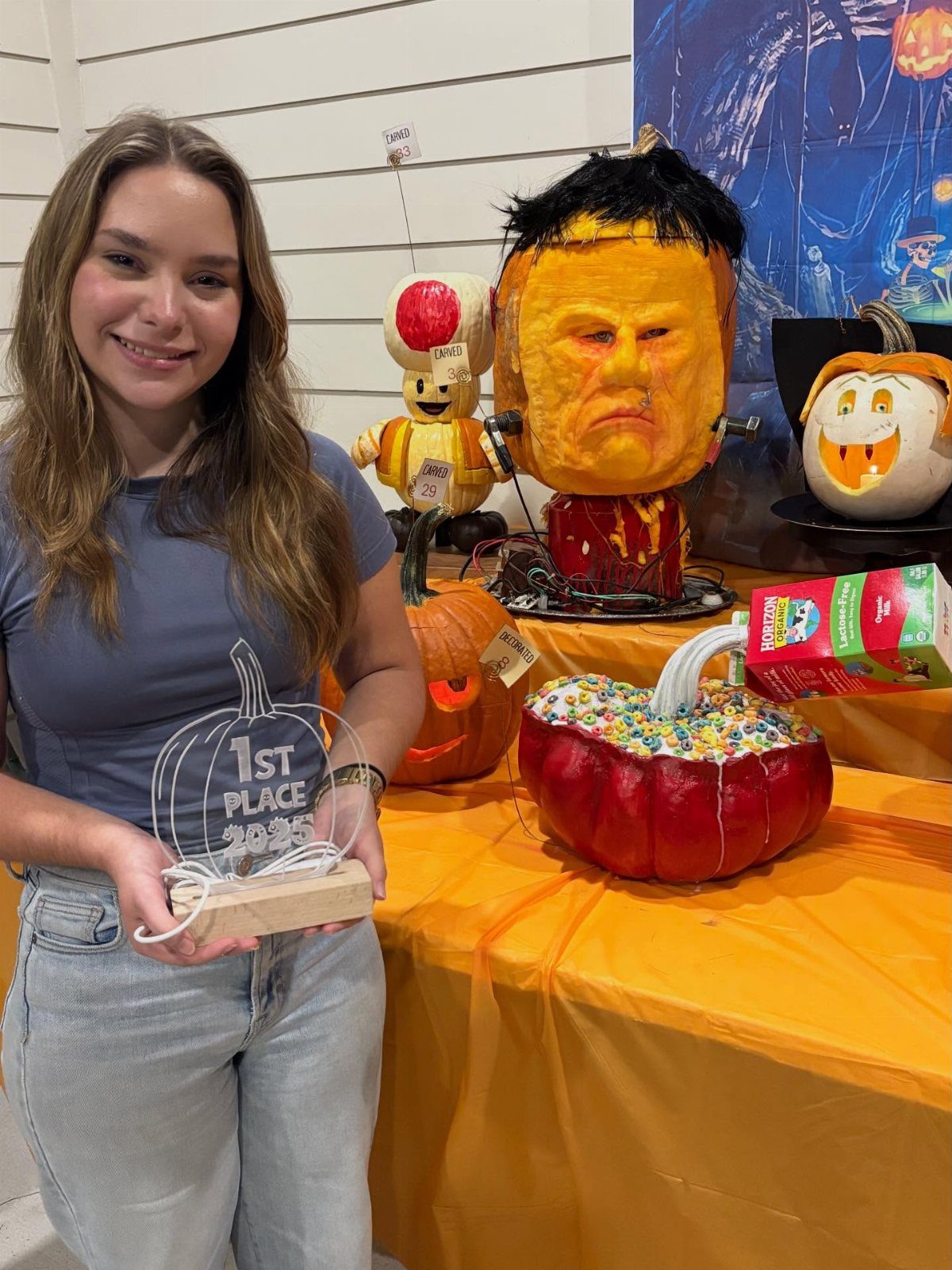 Young woman holding a first place trophy next to carved Halloween pumpkins.