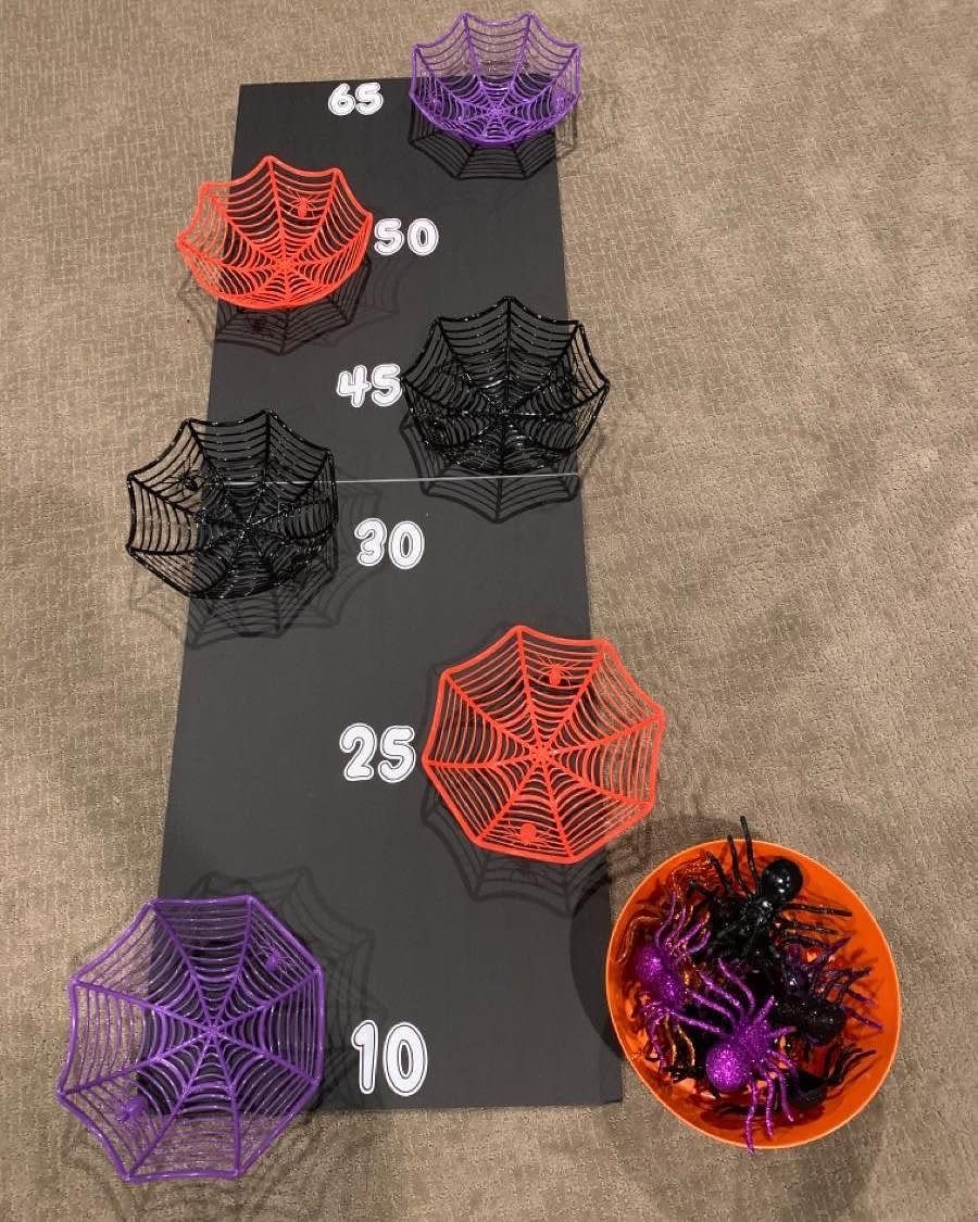 Black game board with colorful plastic spider webs and a bowl of plastic spiders.