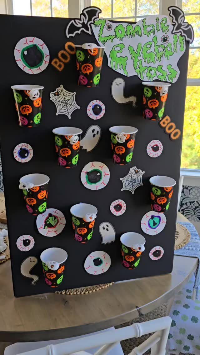 Zombie Eyeball Toss game board with Halloween cups, ghosts, and paper eyeballs.