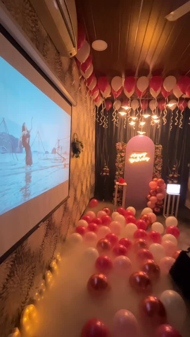 Birthday party room decoration with pink balloons, a projector screen, and neon signage.