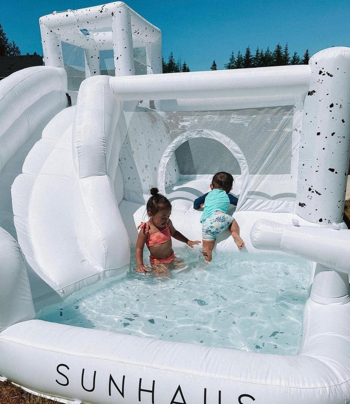 Two children playing in a white inflatable water slide and pool outdoors.