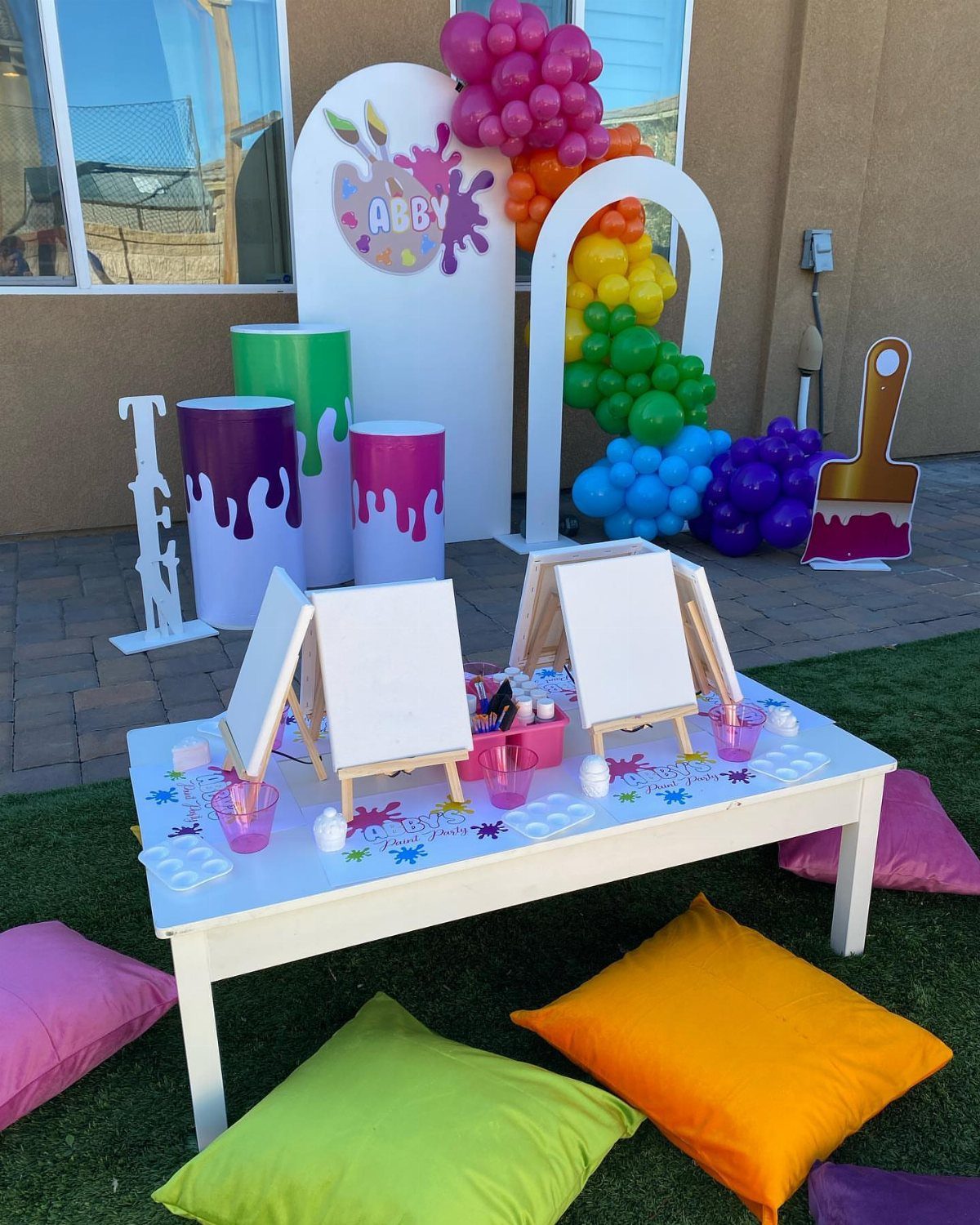 Art party setup with mini canvases on a white table and colorful balloons.
