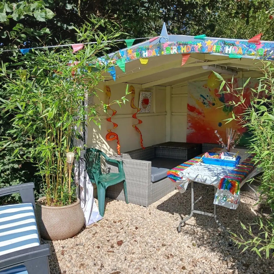 Outdoor birthday party setup in a garden gazebo with colorful decorations and furniture.