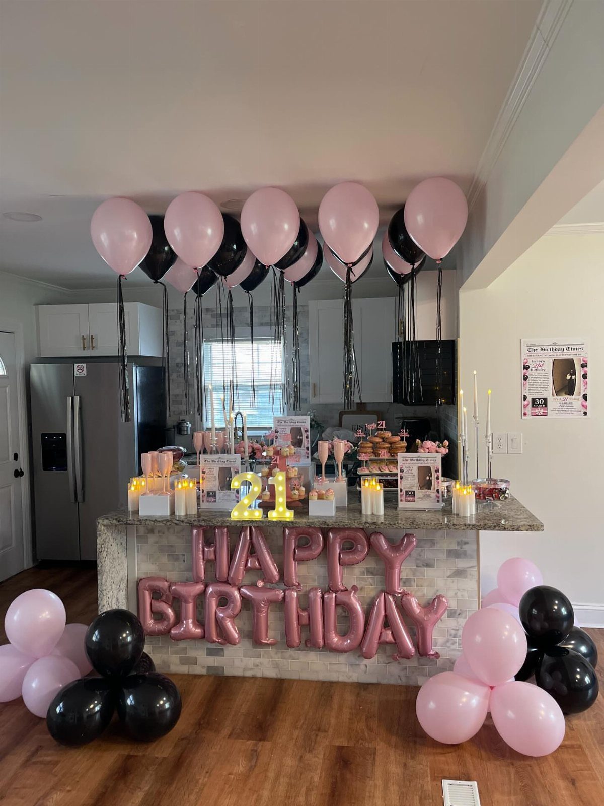 Birthday party setup in a kitchen with pink and black balloons and desserts.