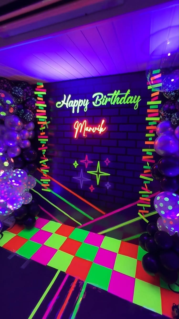 Neon birthday party setup with glowing text, colorful balloons, and checkered floor.