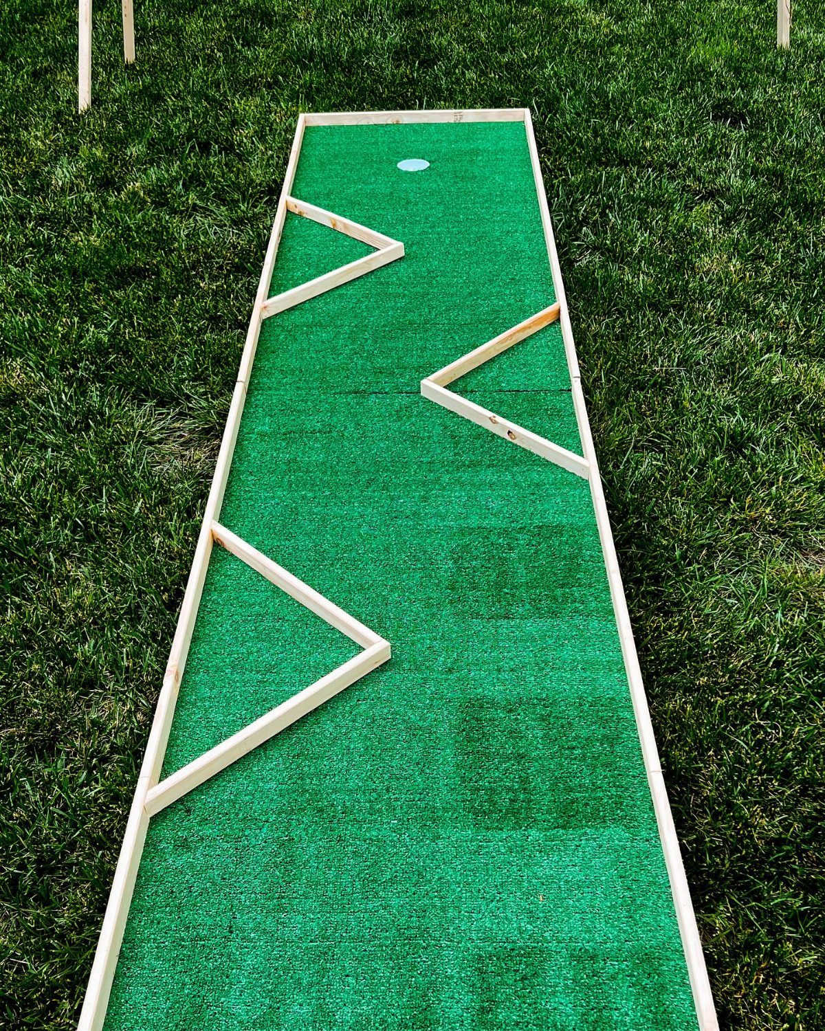 Mini-golf course with green turf and wooden borders on a grassy lawn.