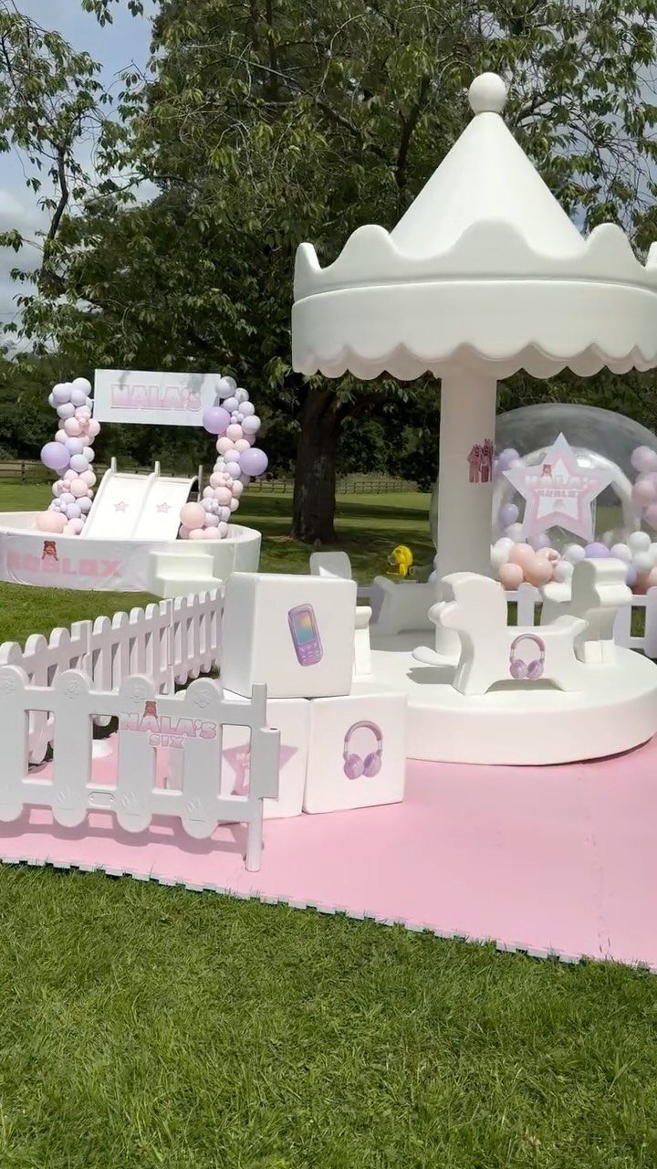White carousel and balloon decorations on a pink mat for a kids birthday party.