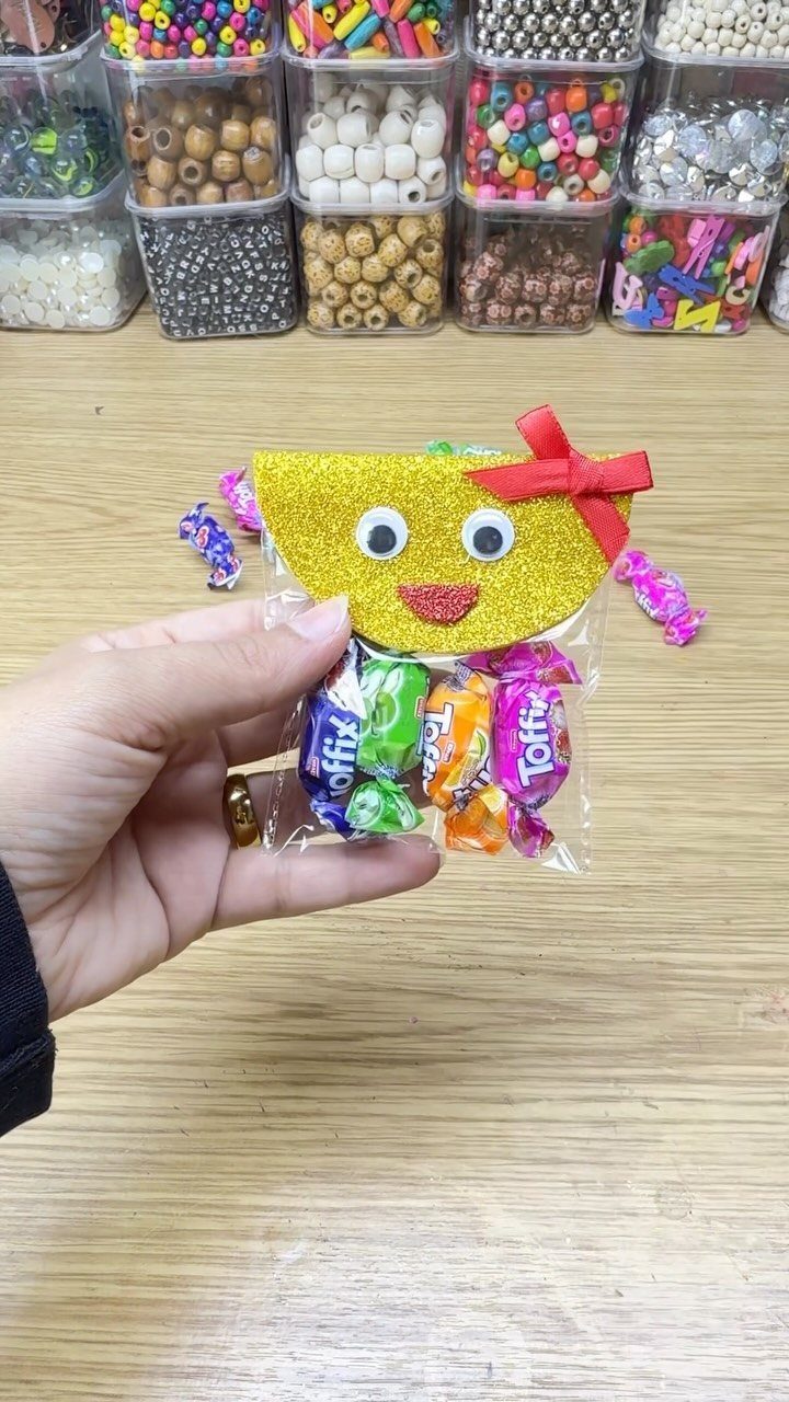 Hand holding a candy bag with a glittery chick face near bead bins.