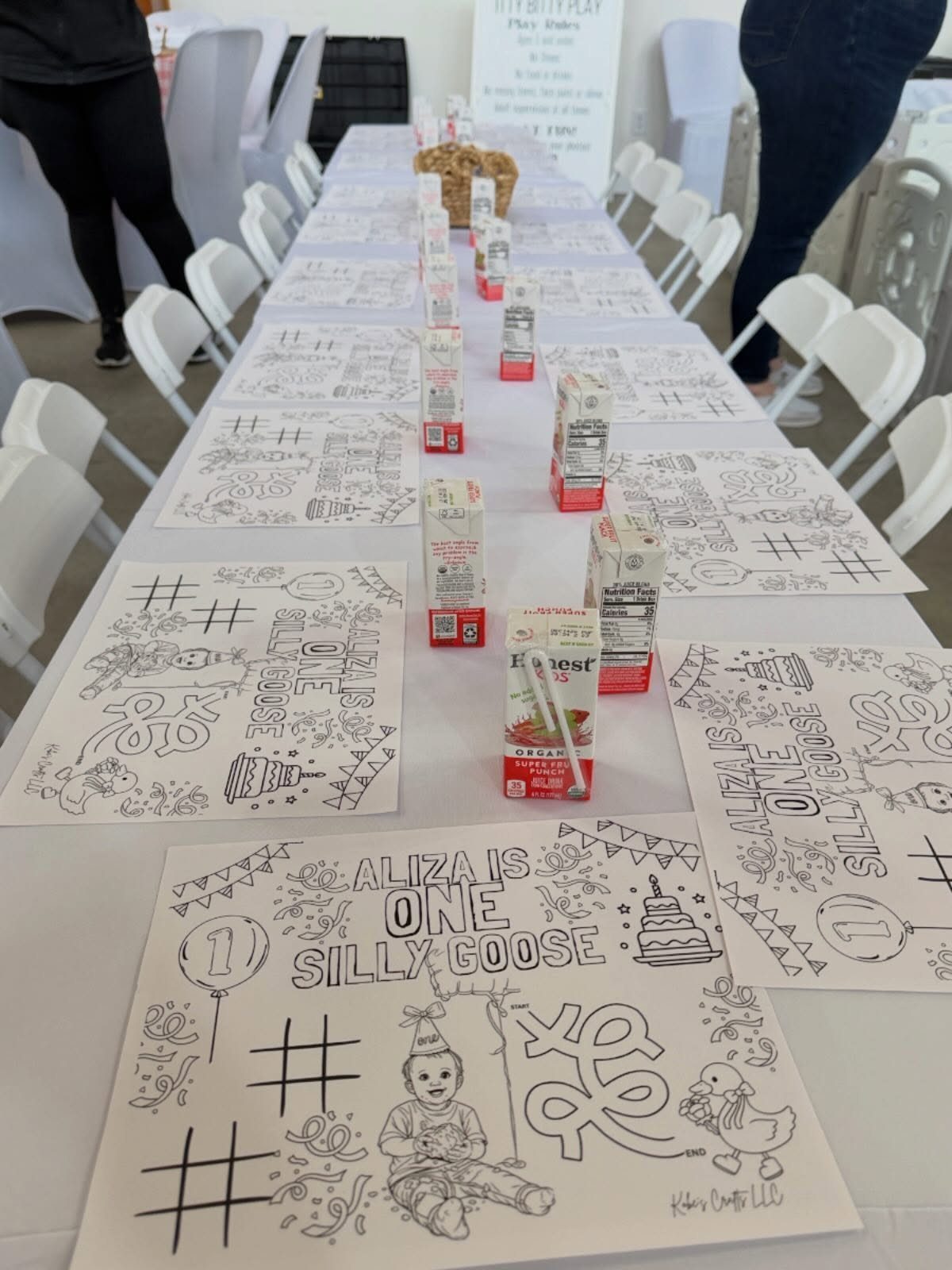 Coloring pages and juice boxes arranged on a long white table for kids.
