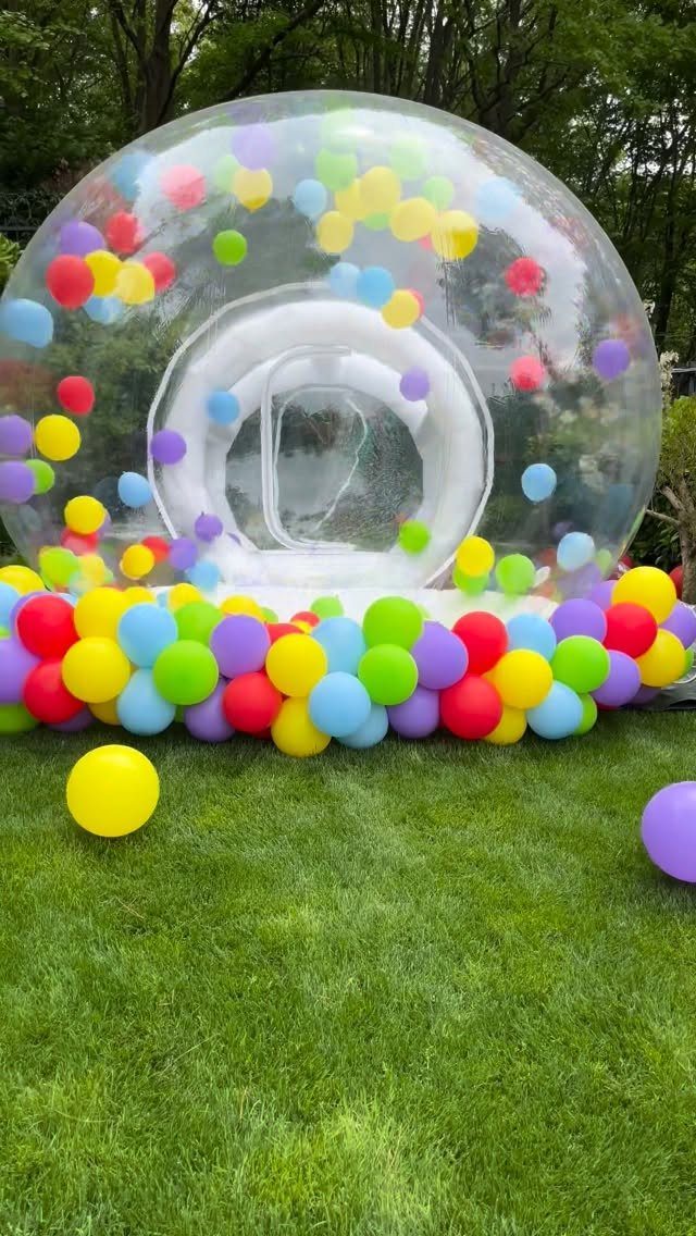 Clear inflatable bubble dome filled with colorful balloons on a green grass lawn