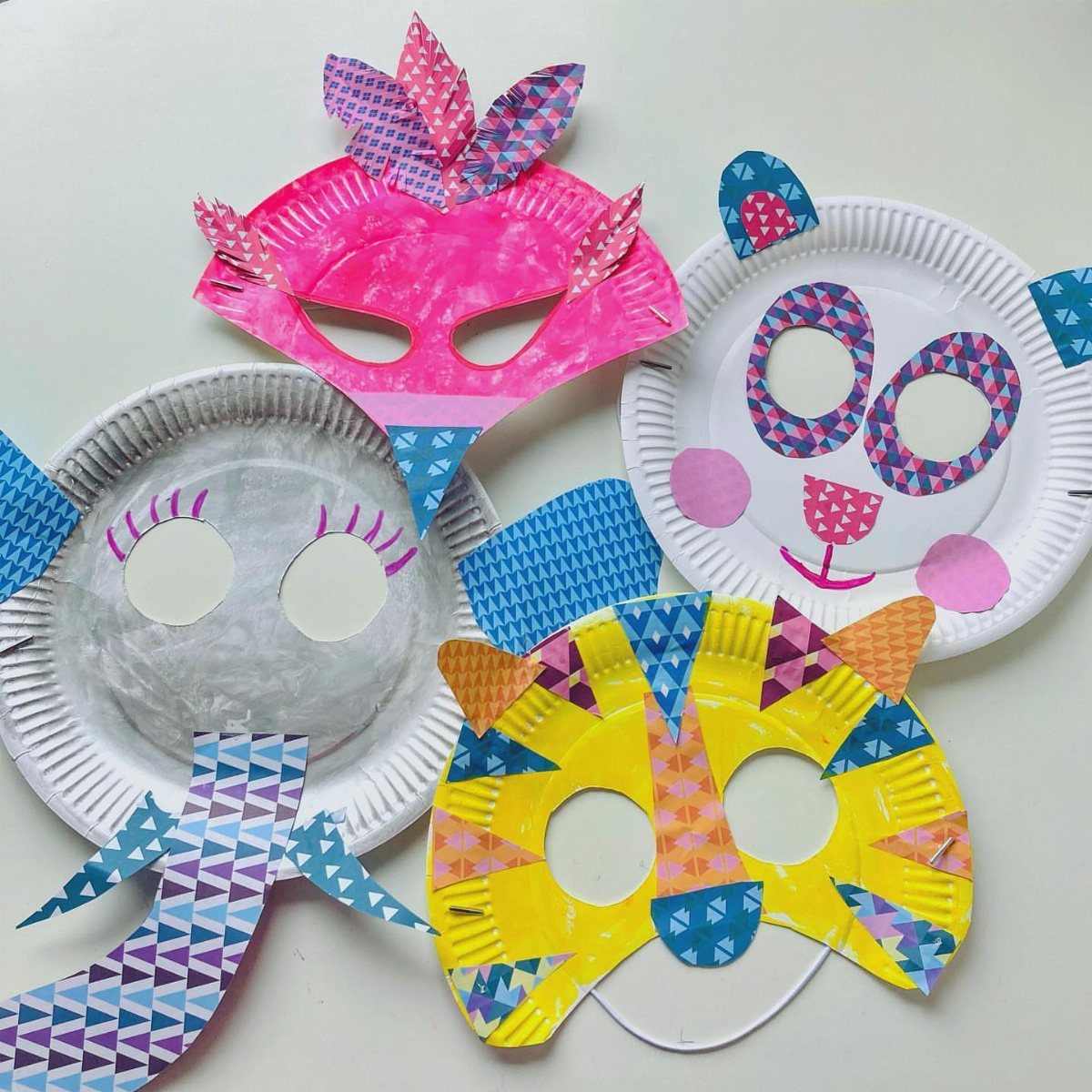 Colorful animal masks crafted from paper plates with patterned paper decorations on white background