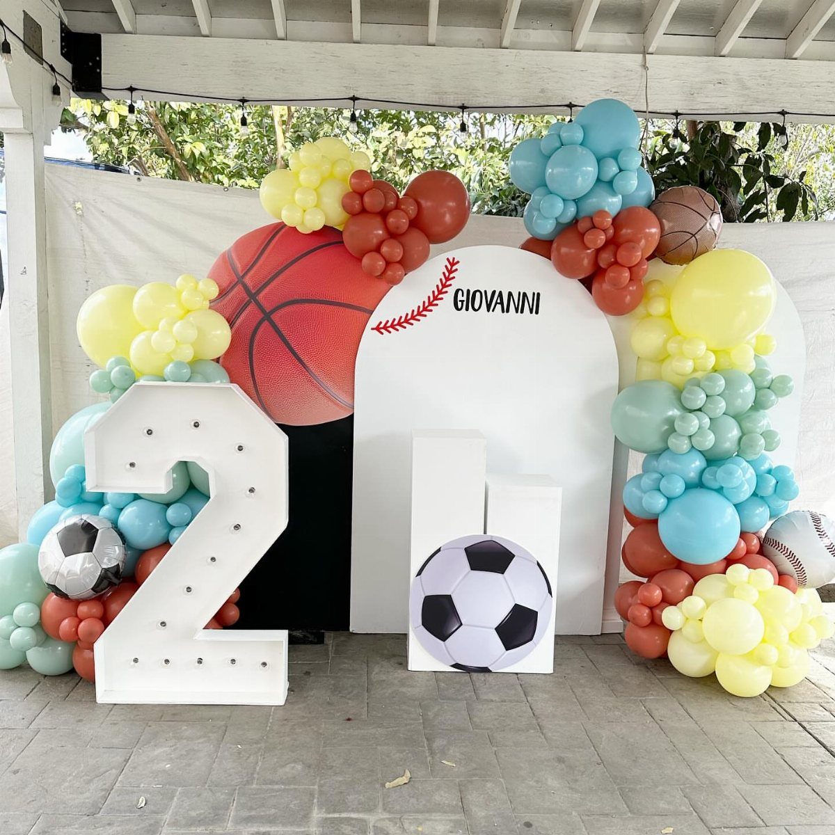 Sports themed party backdrop with large number 2, balloons, and sports ball decorations.