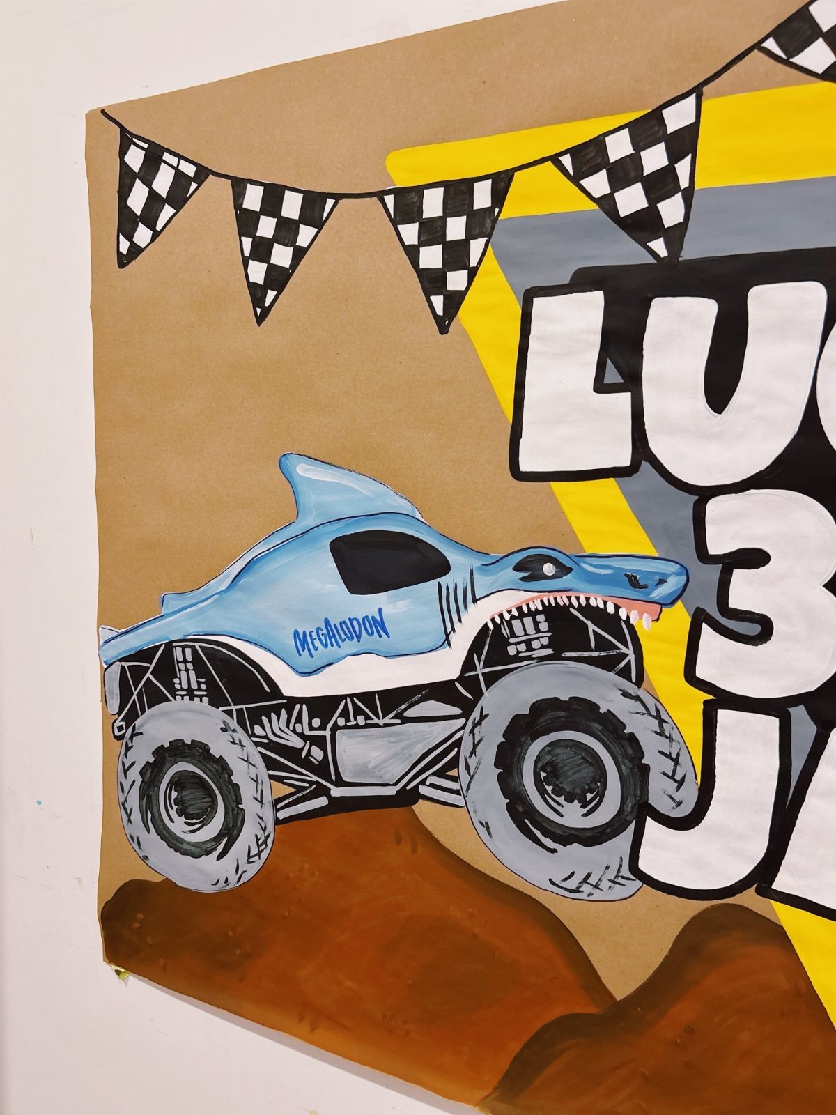 Hand-painted birthday banner featuring a blue shark monster truck and checkered flags.