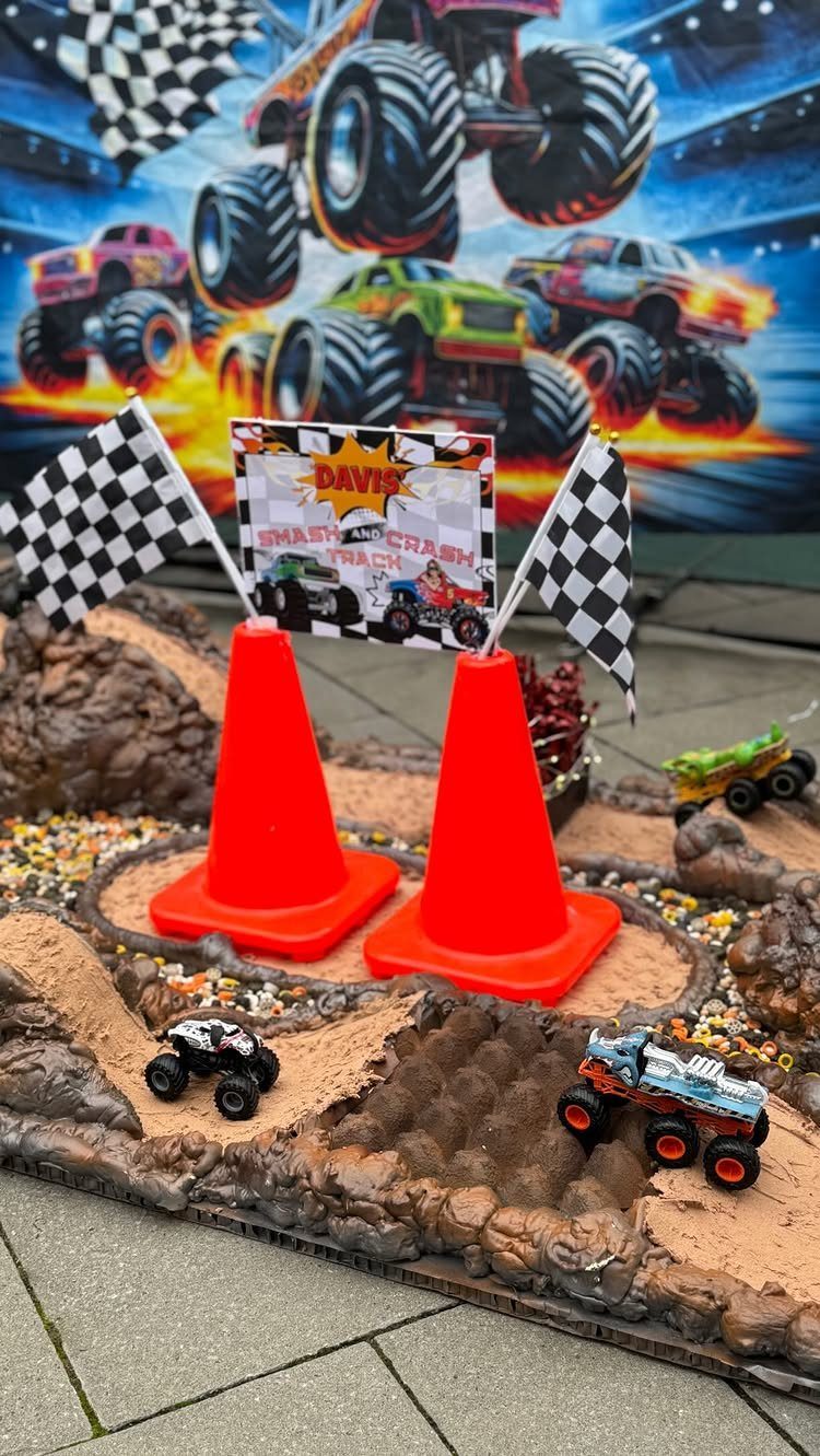 Miniature monster truck track with orange cones, checkered flags, and toy trucks.