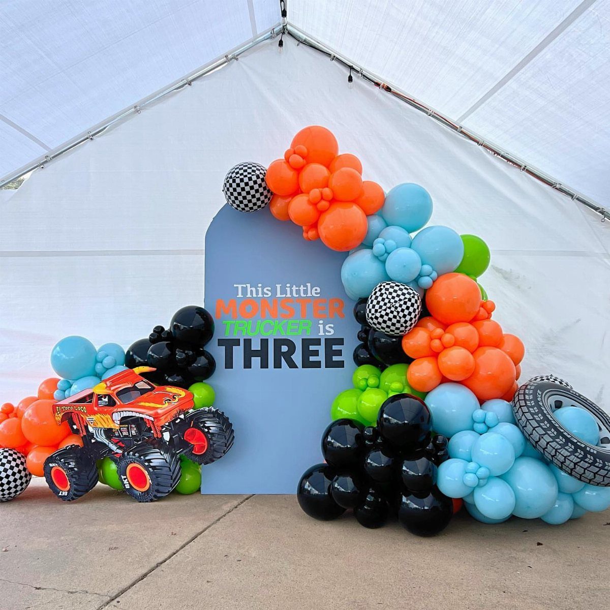 Colorful balloon arch and monster truck backdrop for a third birthday party celebration.