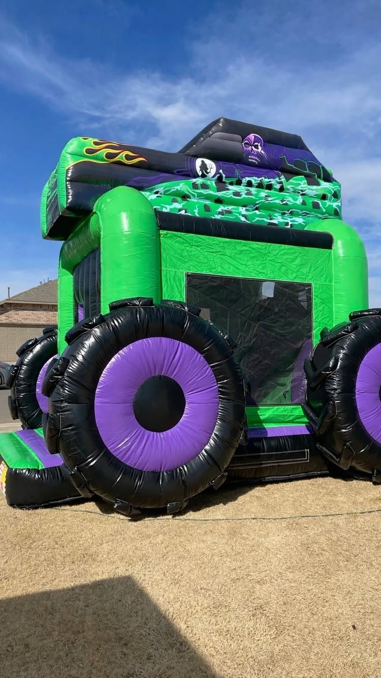 Green monster truck inflatable bounce house with large purple and black tires outdoors.