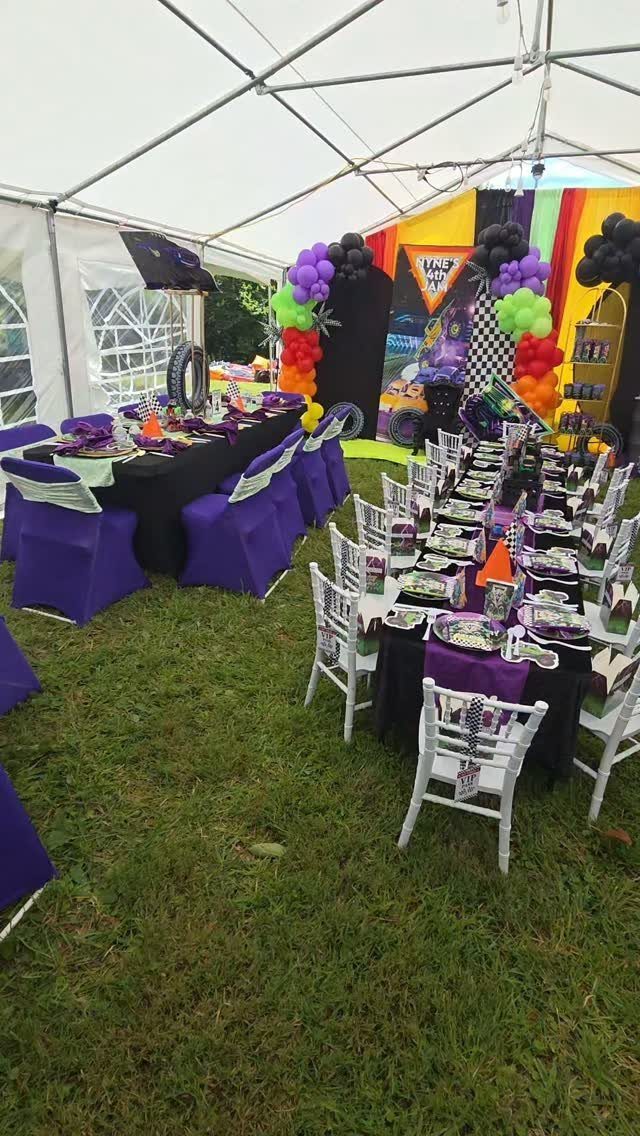 Party tables with purple linens and colorful balloon clusters under a white tent.